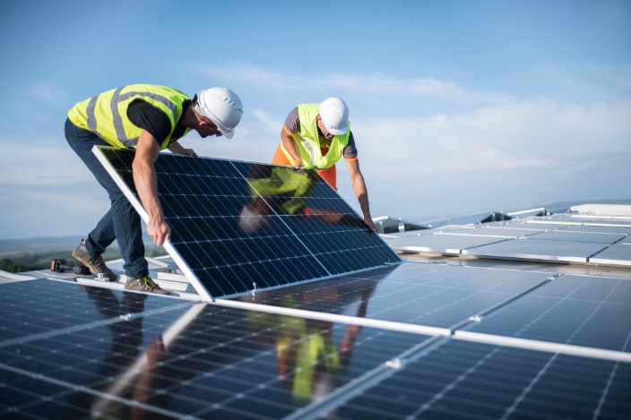 Zwei Monteure installieren eine Solaranlage auf einem Dach.