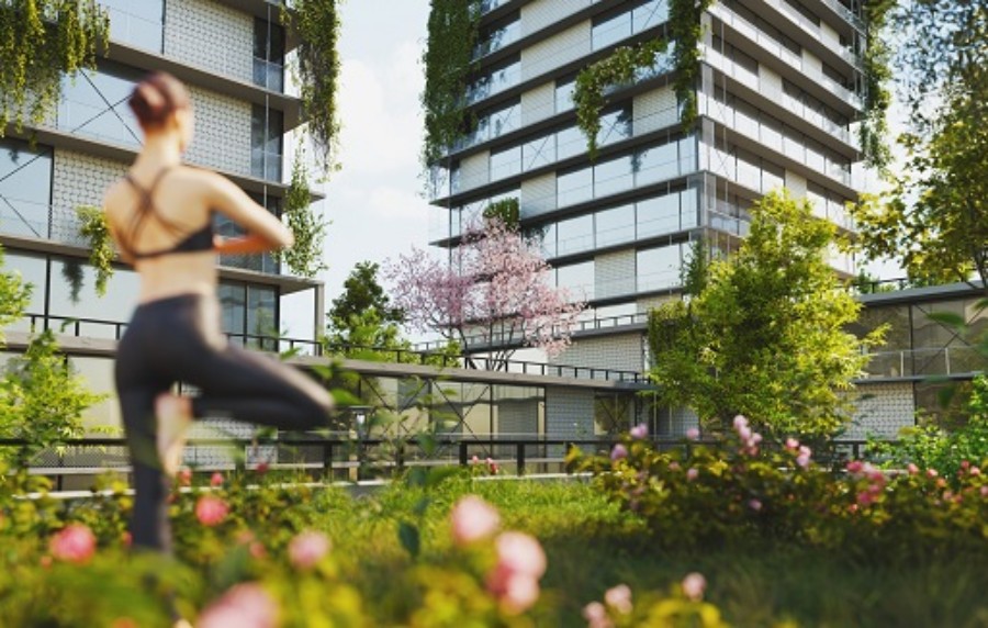 Eine junge Frau macht draußen im Grünen einer Wohnanlage Yoga.